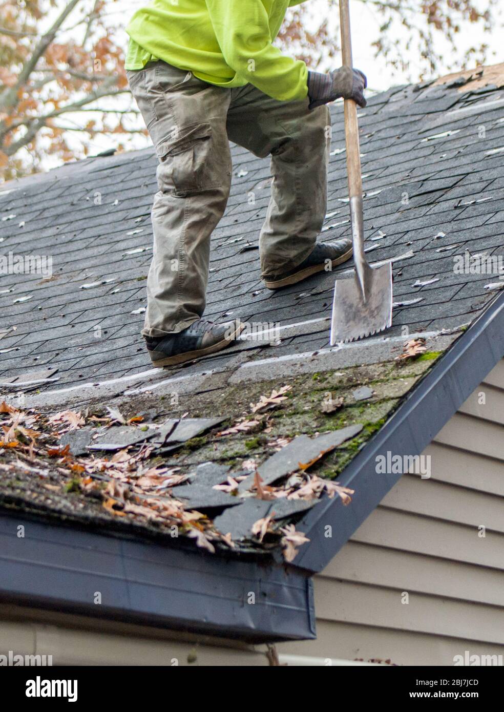 Worker on a roof top uses a special tool to remove old shingles from