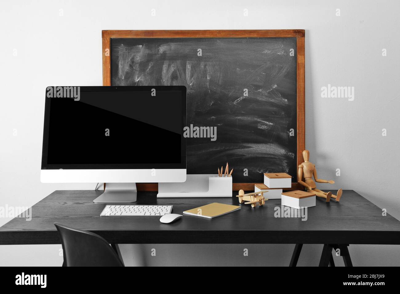 Desktop with computer monitor and other items against blackboard