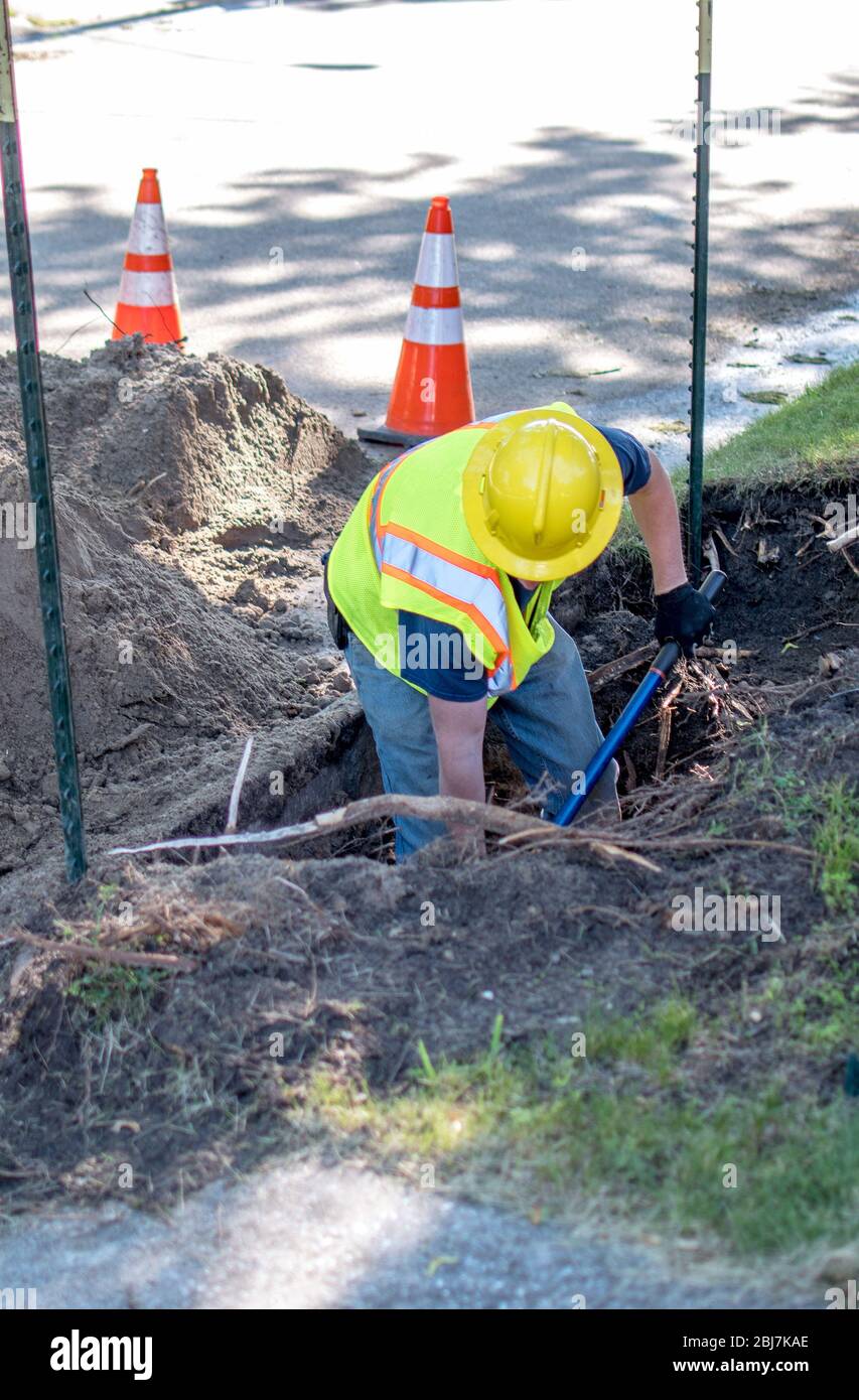 Worker digs to reach a buried cable outside a city home, so he can fix the problem Stock Photo