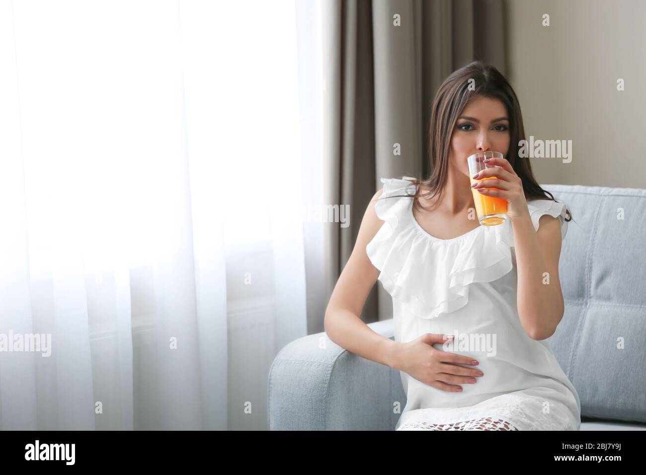 Pregnant woman drinking orange juice in the room Stock Photo - Alamy