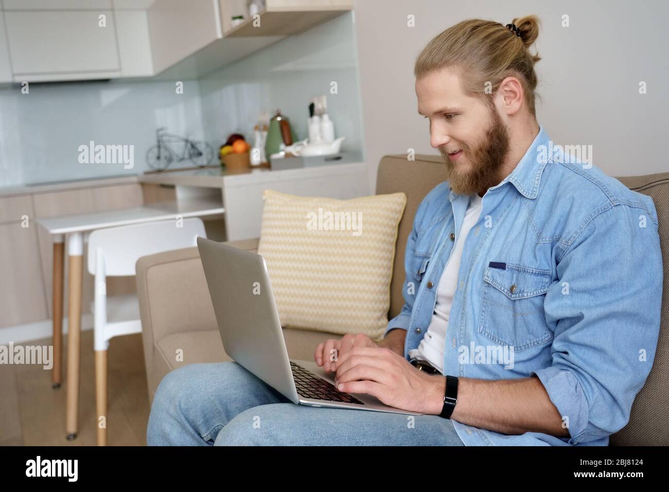 Young man elearning from home using laptop sitting on sofa during quarantine. Stock Photo