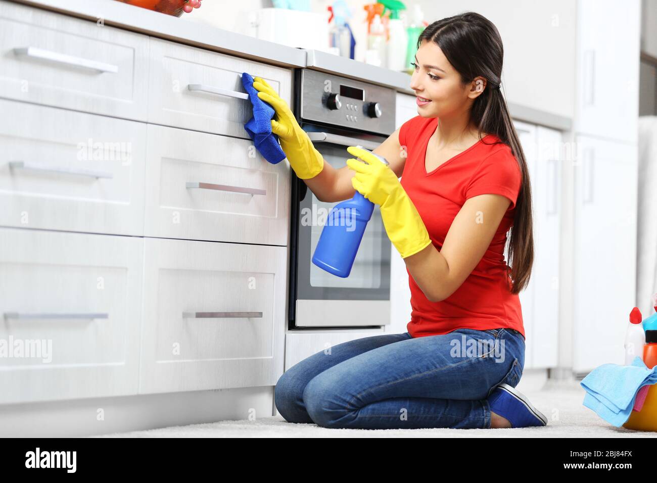 Beautiful woman in protective gloves cleaning kitchen cabinet Stock Photo