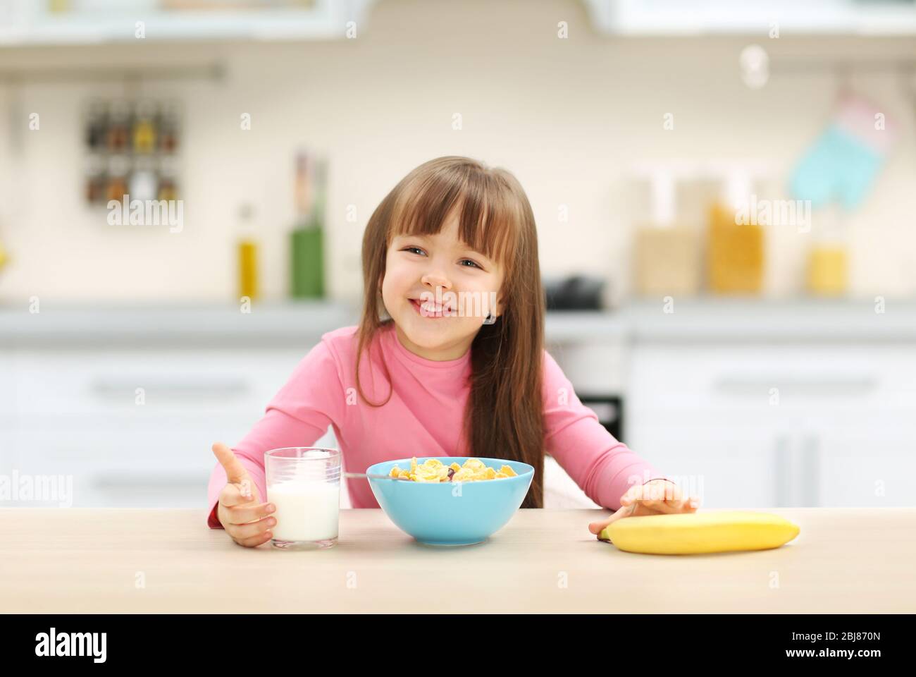 Breakfast Little Beautiful little girl having breakfast with cereal, milk and banana in ...