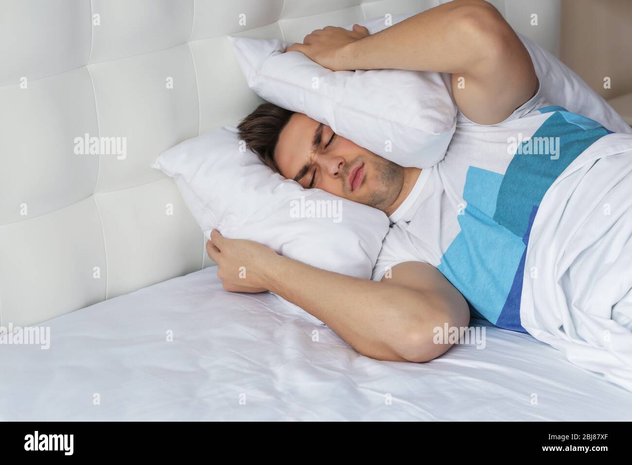 Young man closing his ears with pillows from alarm sound Stock Photo