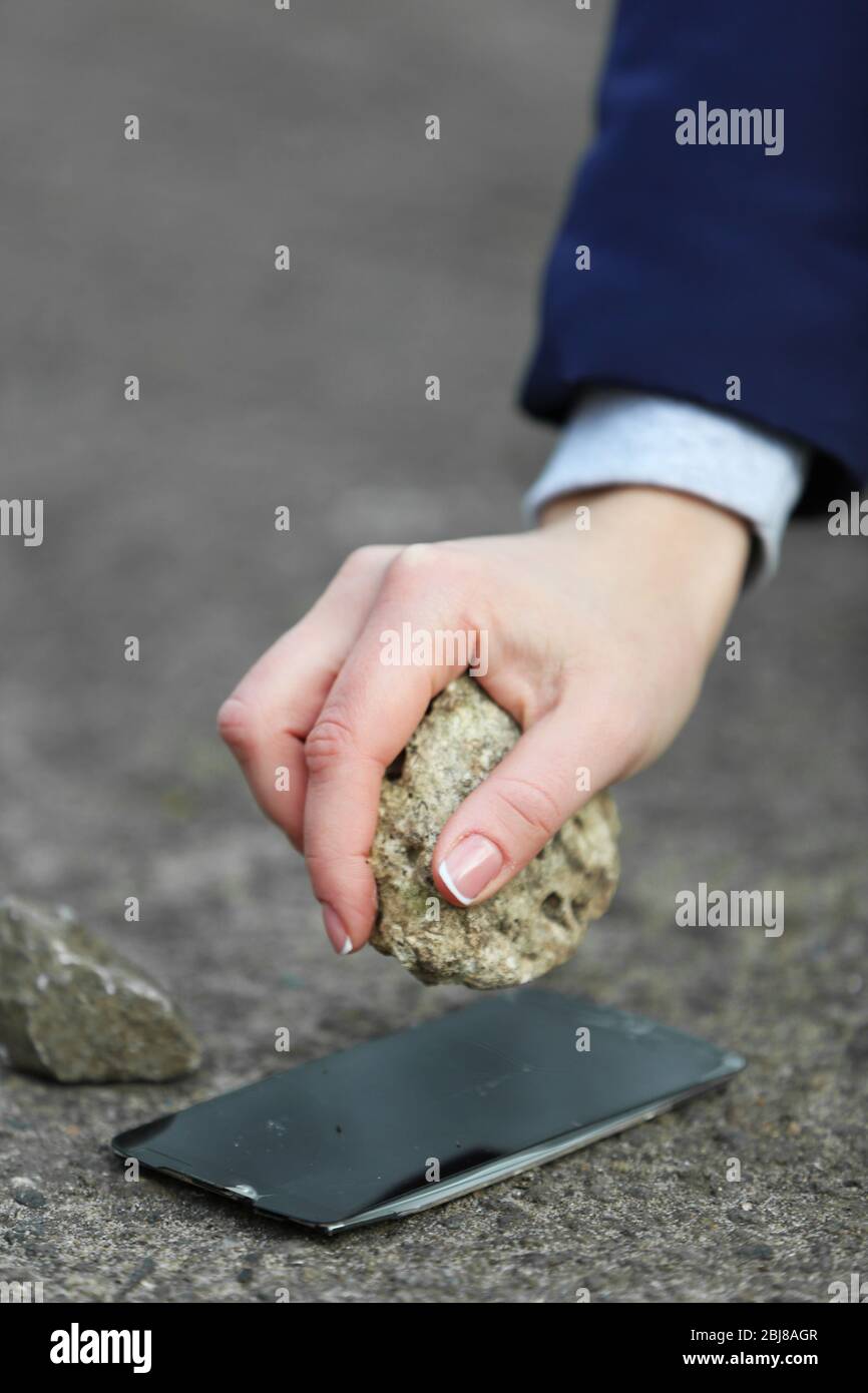 Female hand crushing with stone screen of mobile phone on the pavement