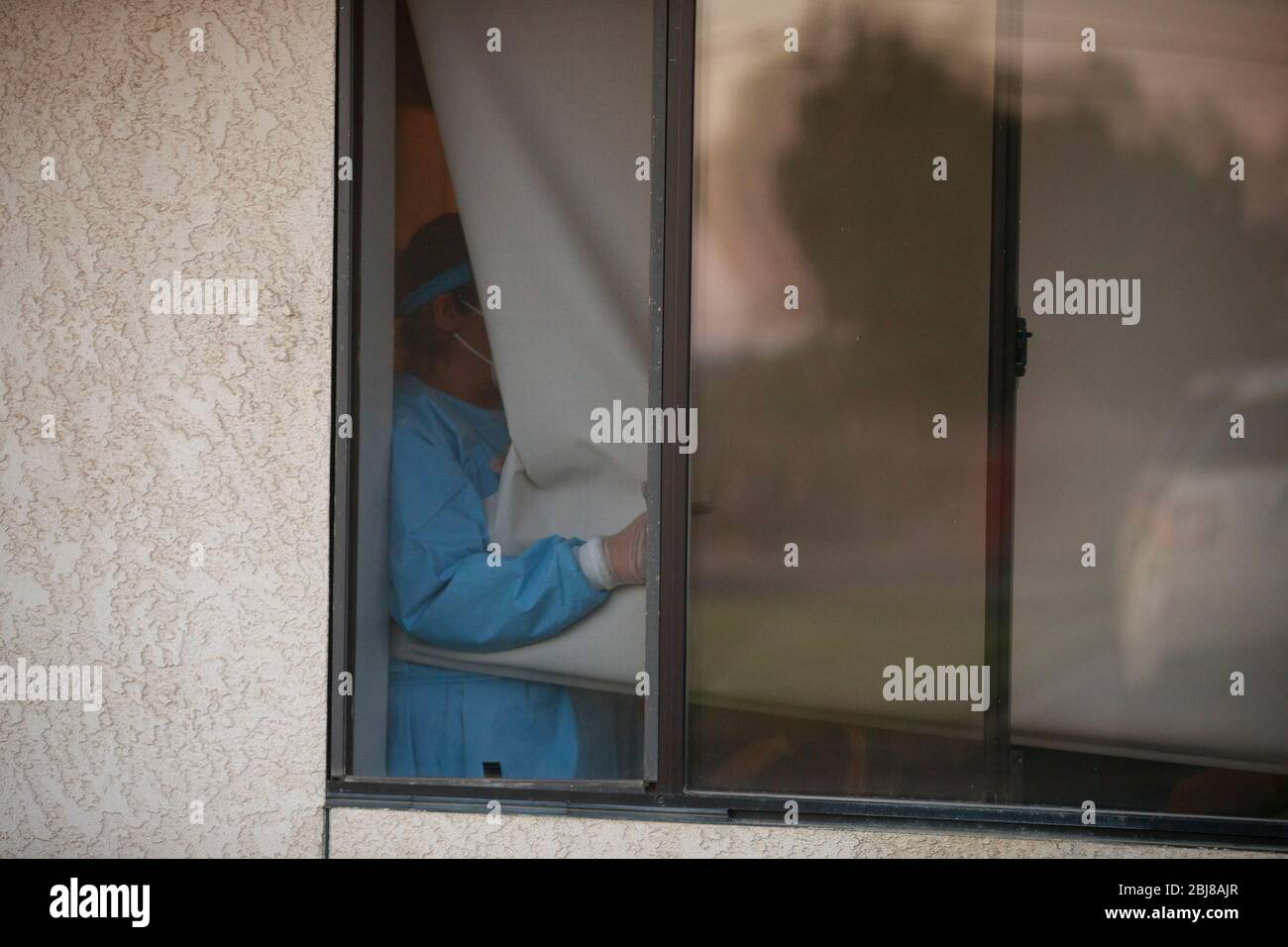 Porterville, United States. 27th Apr, 2020. A worker opens a window so that the family members can visit Jerry Hogan, a Vietnam Veteran, who is lying on a bed at Lindsey Gardens after testing positive for COVID-19/Coronavirus, a week earlier. Hogan had been in the hospital, where he had pneumonia unrelated to Coronavirus, and had tested negative, when he was sent to a skilled nursing facility for rehabilitation, then there was an outbreak at the facility, where he then tested positive a few days later. Credit: SOPA Images Limited/Alamy Live News Stock Photo
