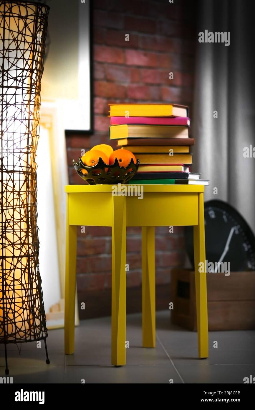Stylish interior with yellow coffee table, books at night Stock Photo