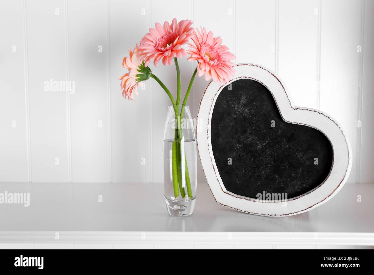 Bouquet of pink gerberas in glass vase with frame on a shelf over white
