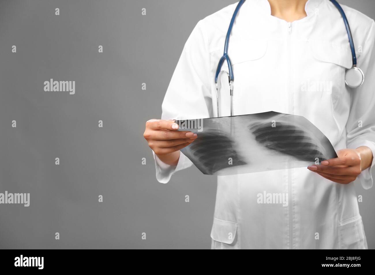 Young female doctor holding radiogram on grey background Stock Photo