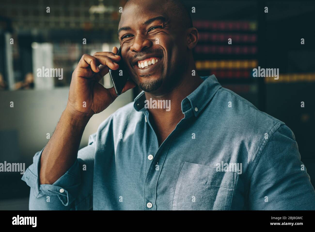 Businessman talking on phone standing in office. Smiling young african man speaking on mobile phone at work. Stock Photo