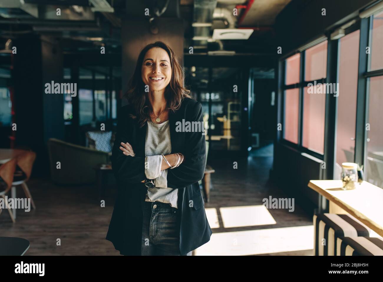 Confident businesswoman standing in office. Smiling woman standing with her arms crossed looking at camera. Stock Photo
