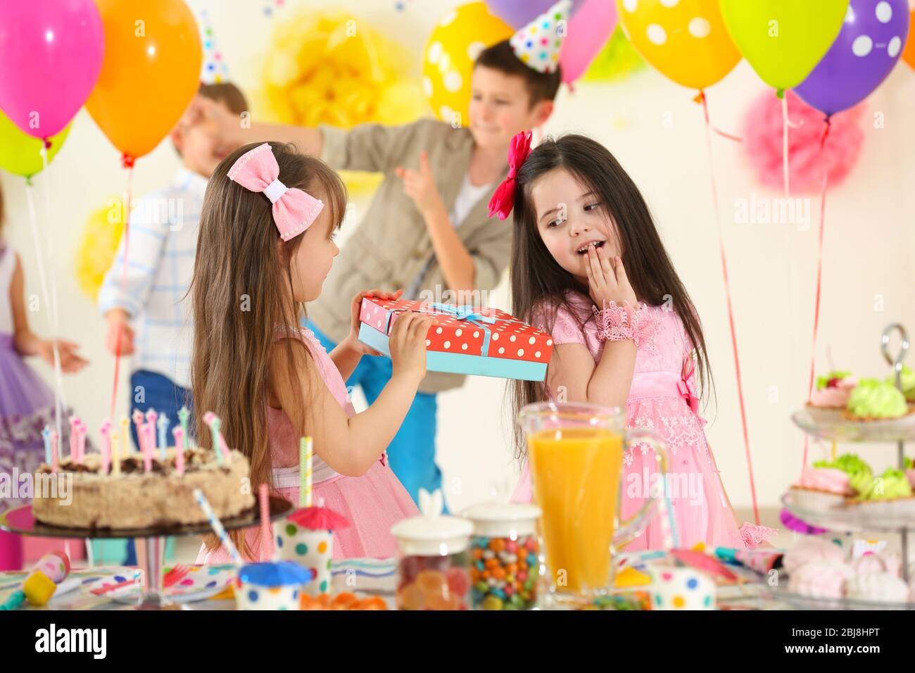 Happy little girl presenting a gift to her friend at birthday party ...