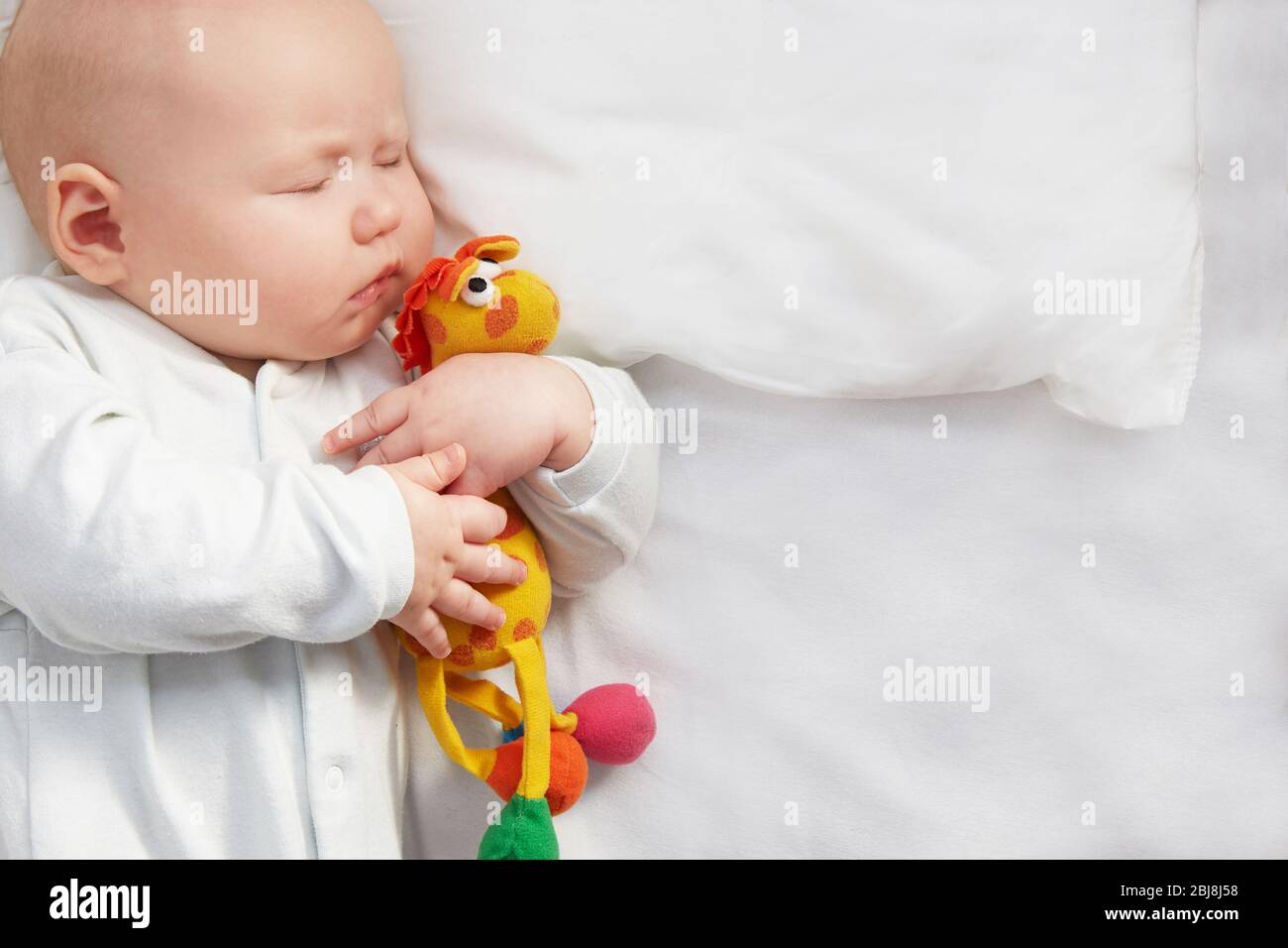Cute baby sleeping with a toy on a white pillow. copyspace. Stock Photo