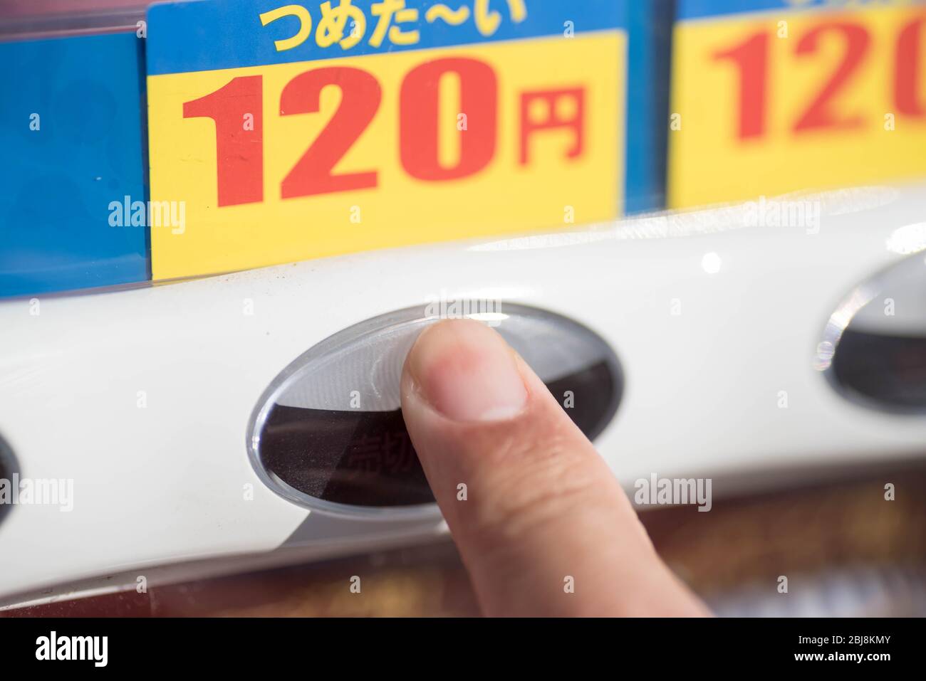 A finger pressing a button on a Japanese vending machine to buy a drink