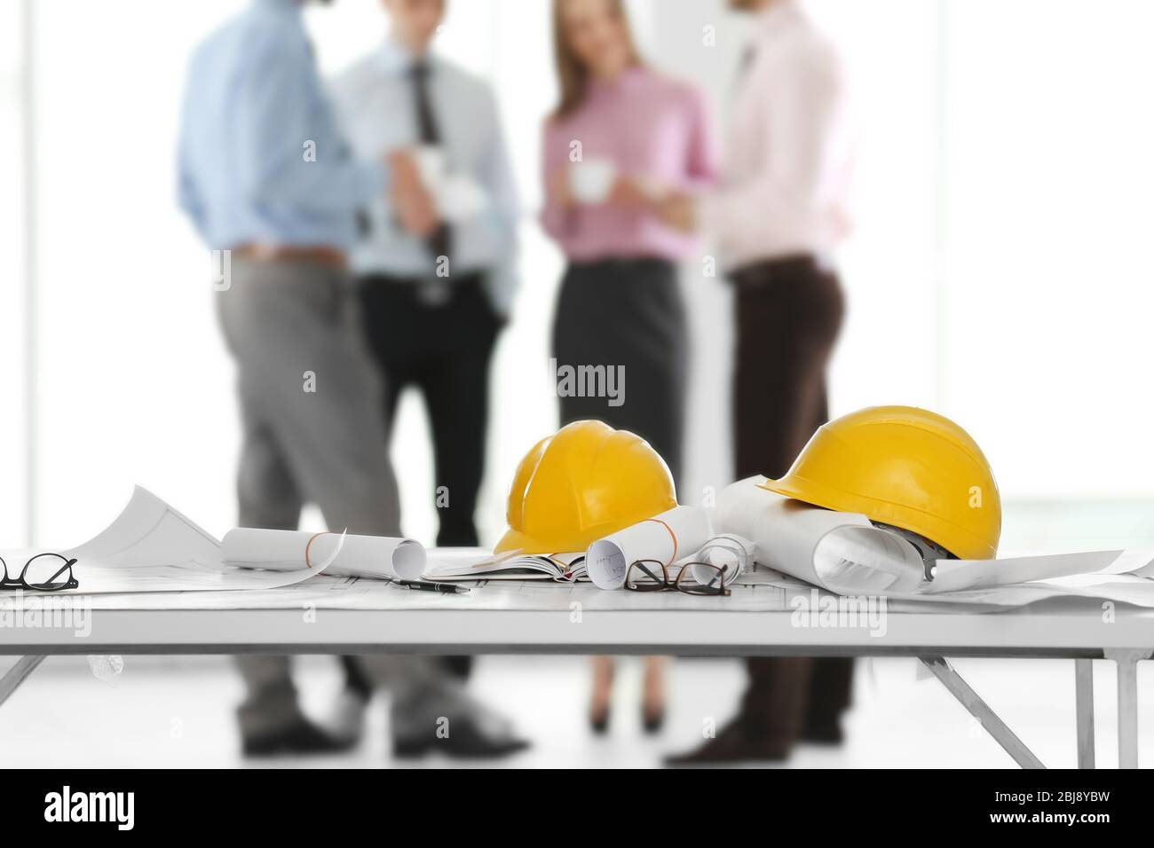 Helmets with blueprints on table and engineers on background Stock Photo