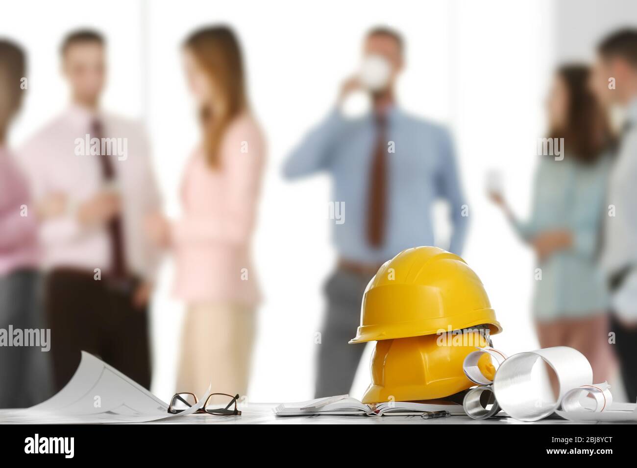 Helmets with blueprints on table and engineers on background Stock Photo