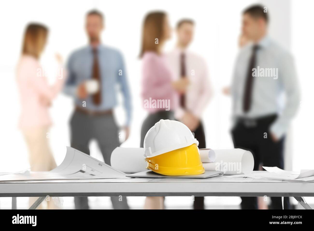 Helmets with blueprints on table and engineers on background Stock Photo