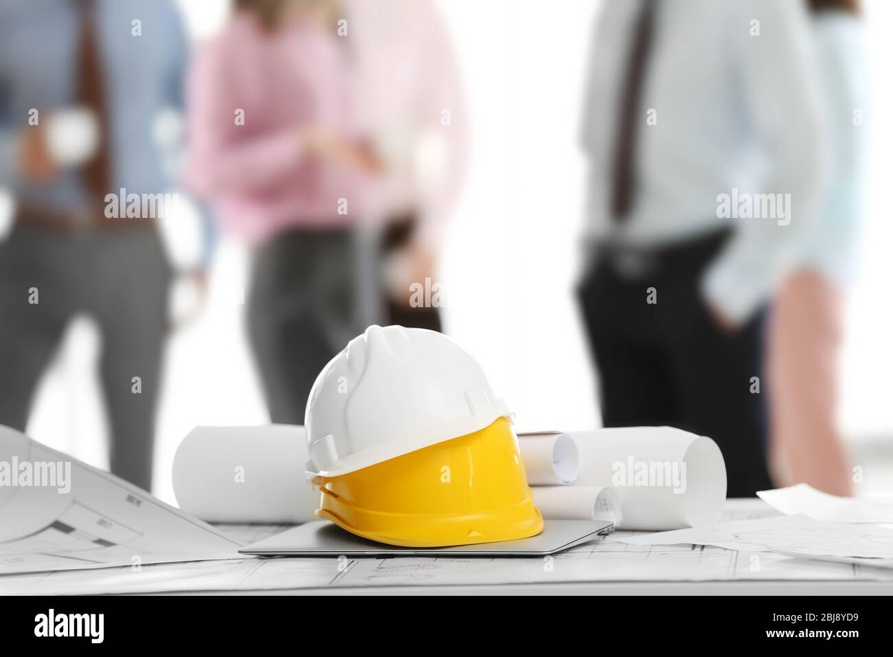 Helmets with blueprints on table and engineers on background Stock Photo