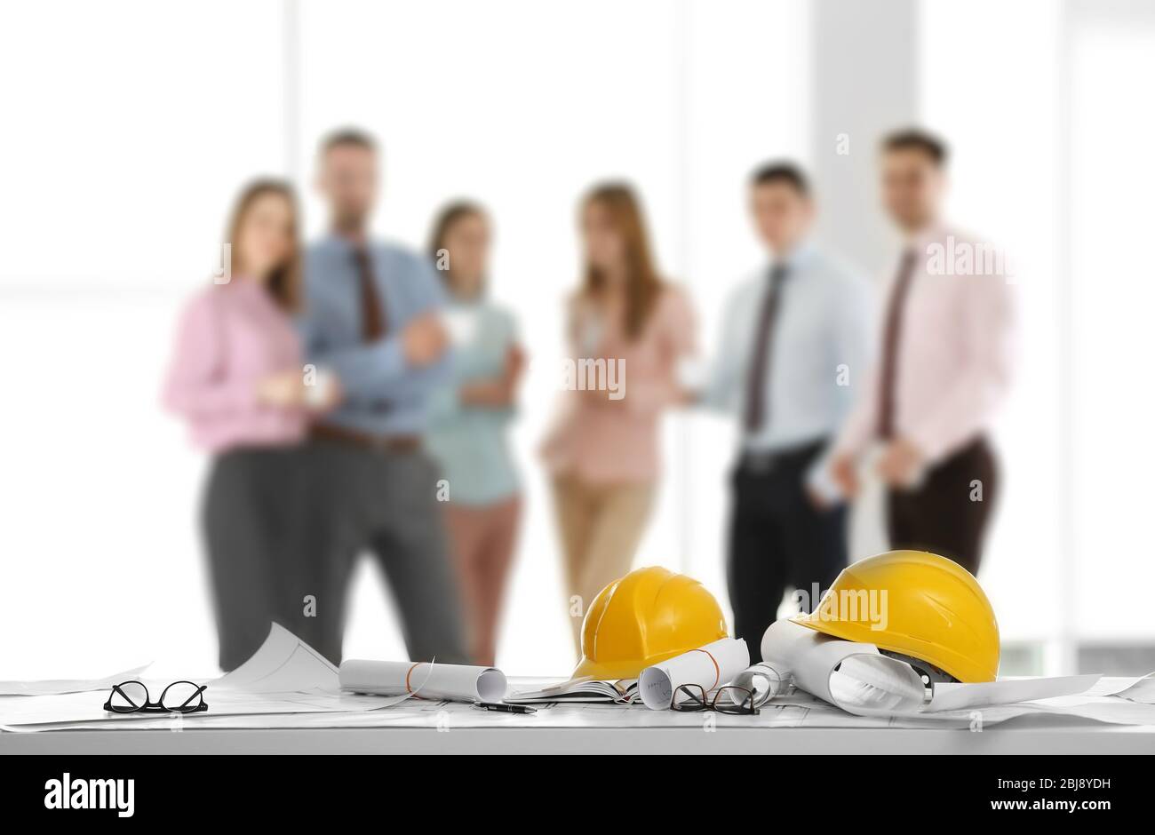 Helmets with blueprints on table and engineers on background Stock Photo