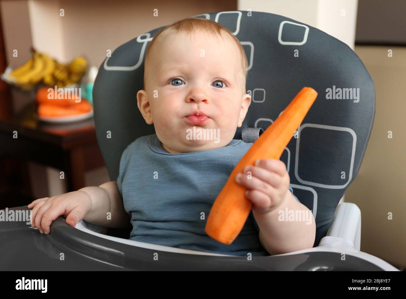 Baby eating carrot in a chair Stock Photo Alamy