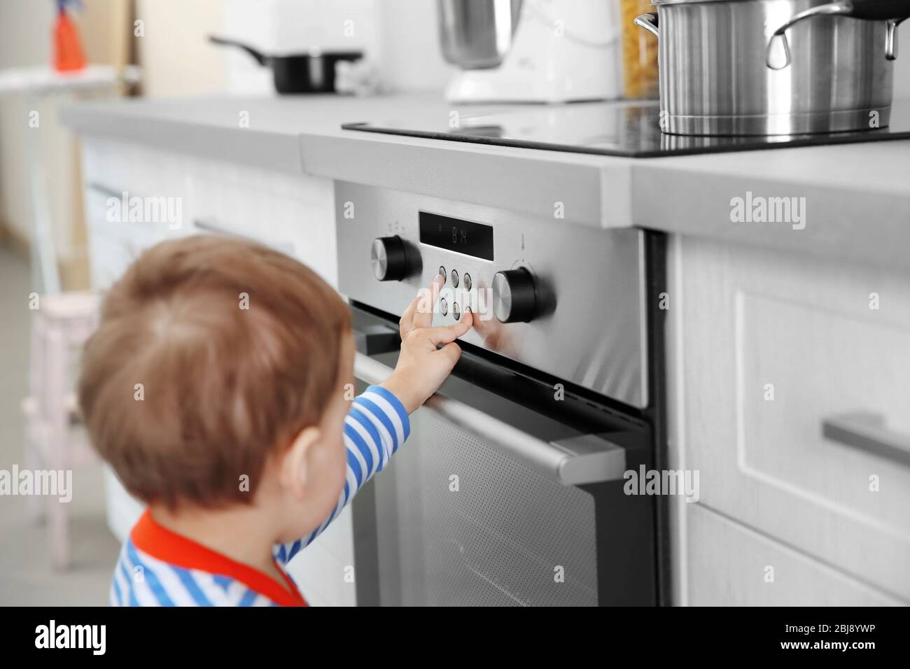 Toddler boy touches hot stove in kitchen. Accident at home with children.  Child pulls a hand to a scorching pan Stock Photo