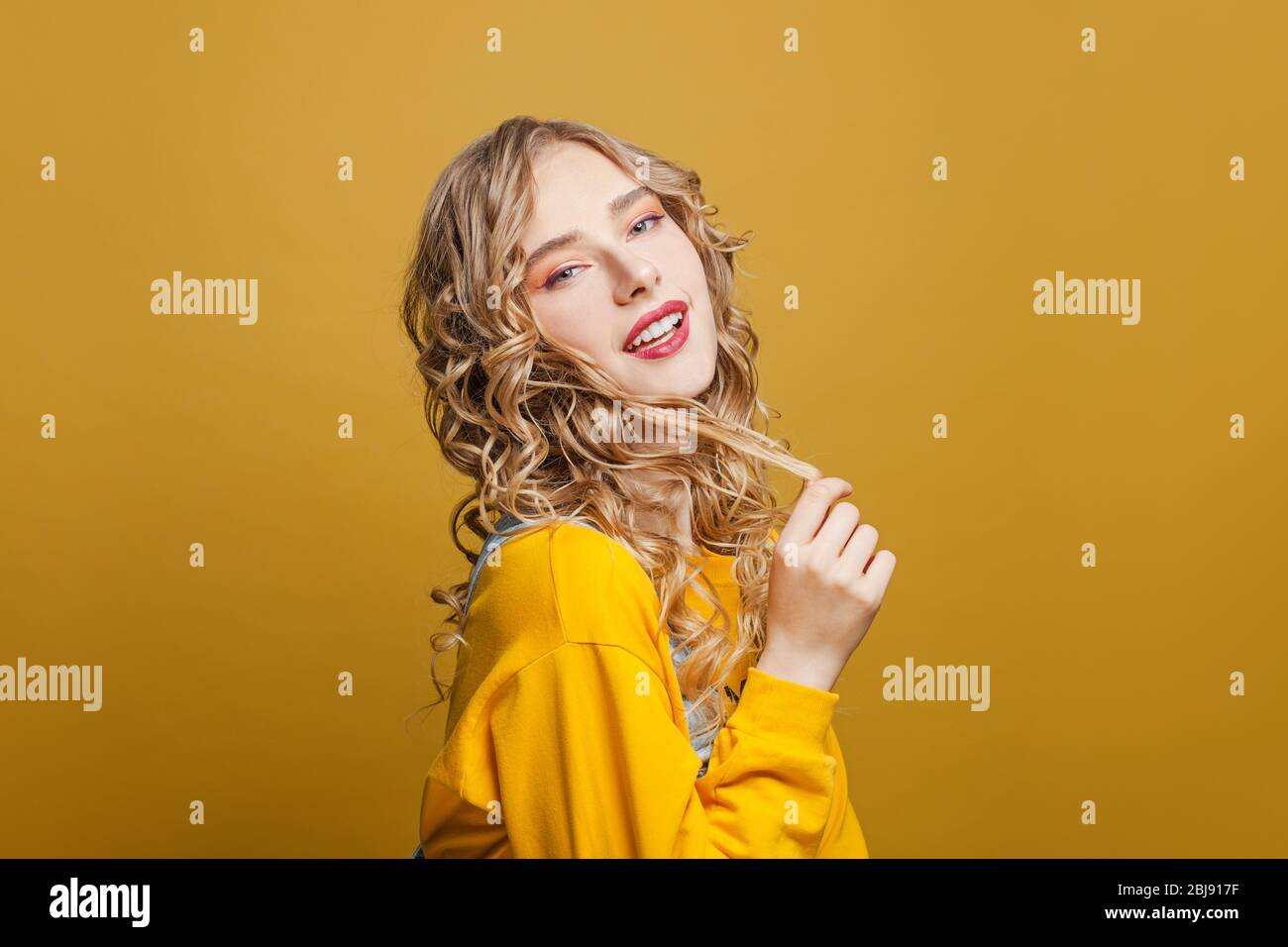 Happy young woman with long blonde curly hair on bright yellow ...