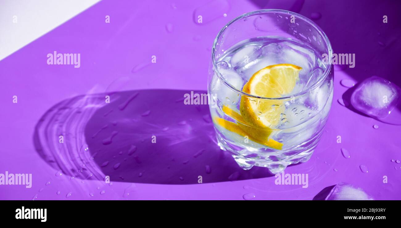 A glass of refreshing water with ice and lemon on a purple background. Heat concept, fresh. Natural light. Flat lay, top view, copy space Stock Photo