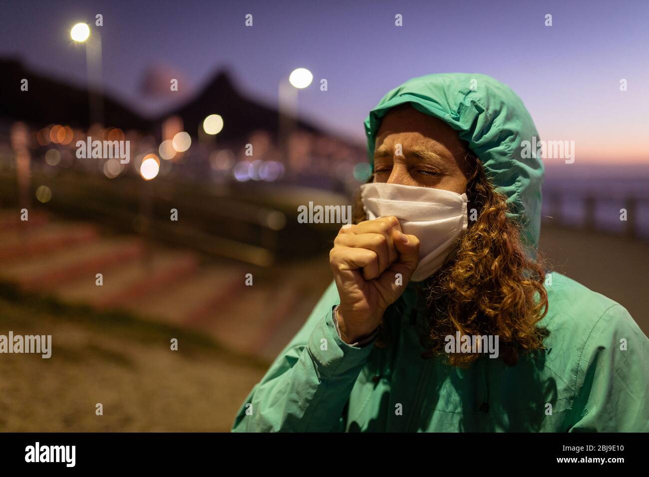 Caucasian woman wearing a protective mask against coronavirus, coughing in the streets Stock Photo
