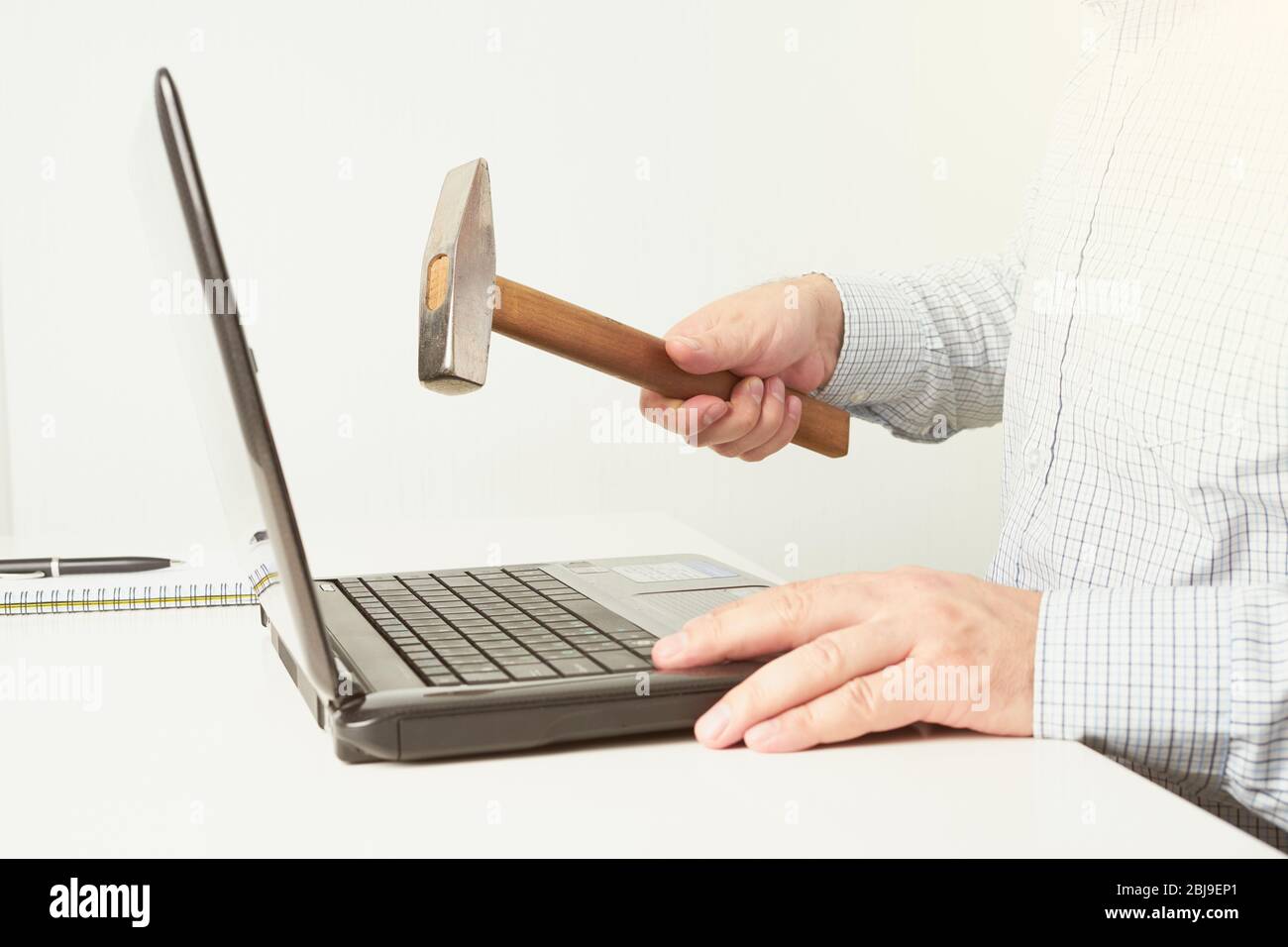 The man raised a hammer over the computer, man in the shirt wants to break the laptop. The concept of fatigue from work Stock Photo