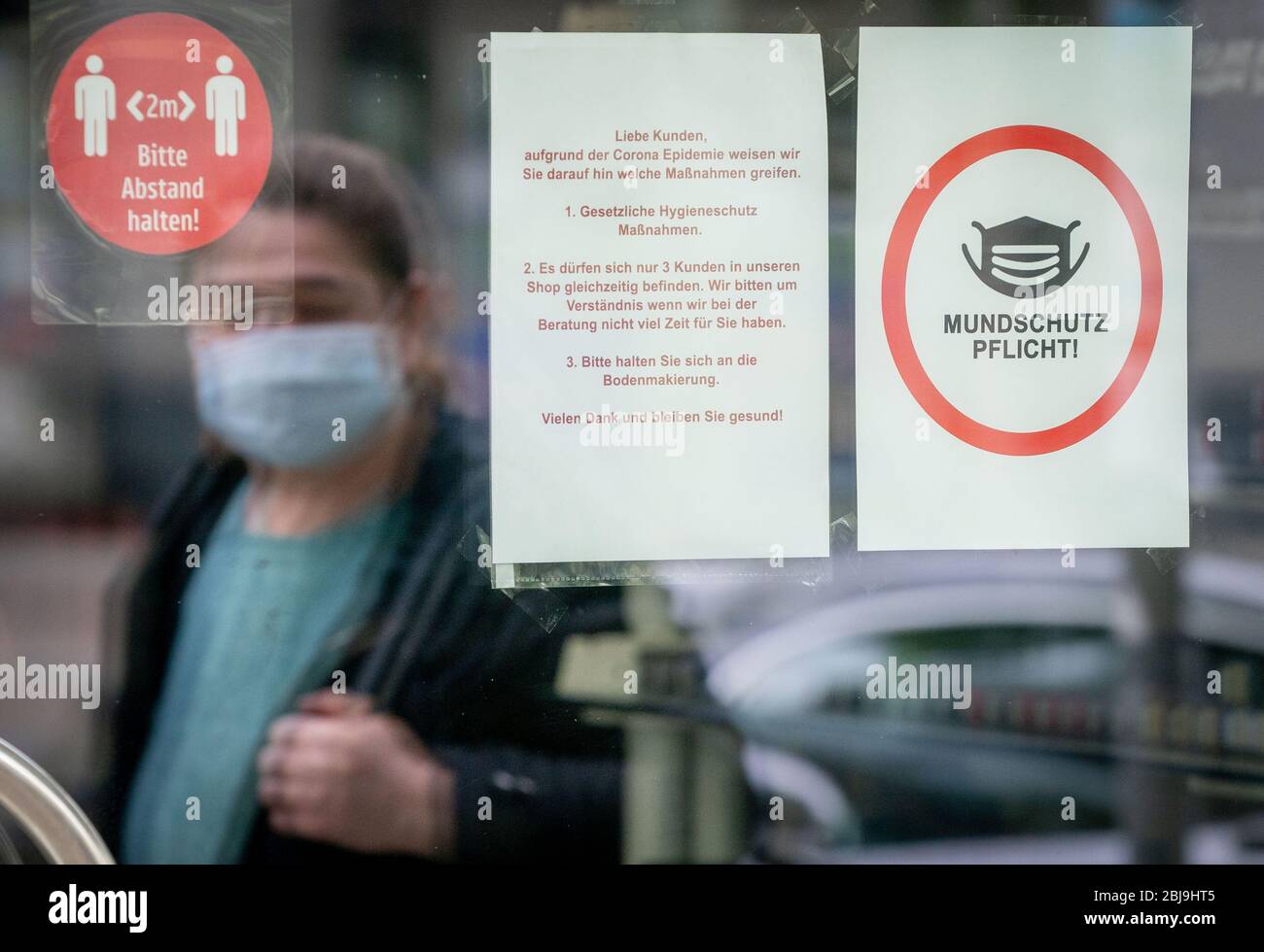 Berlin, Germany. 29th Apr, 2020. A passer-by wearing a mouth-and-nose  protection is reflected in a shop window with a poster saying "Mouth  protection compulsory! Berlin is the last federal state to introduce