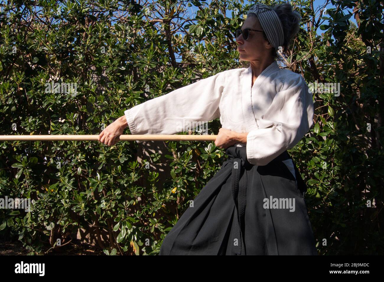 woman training Aikido in her garden during the quarantine. Weapons Aikido training - Aikido Jo kata training - Wearing black belt Aikido clothes - Tra Stock Photo