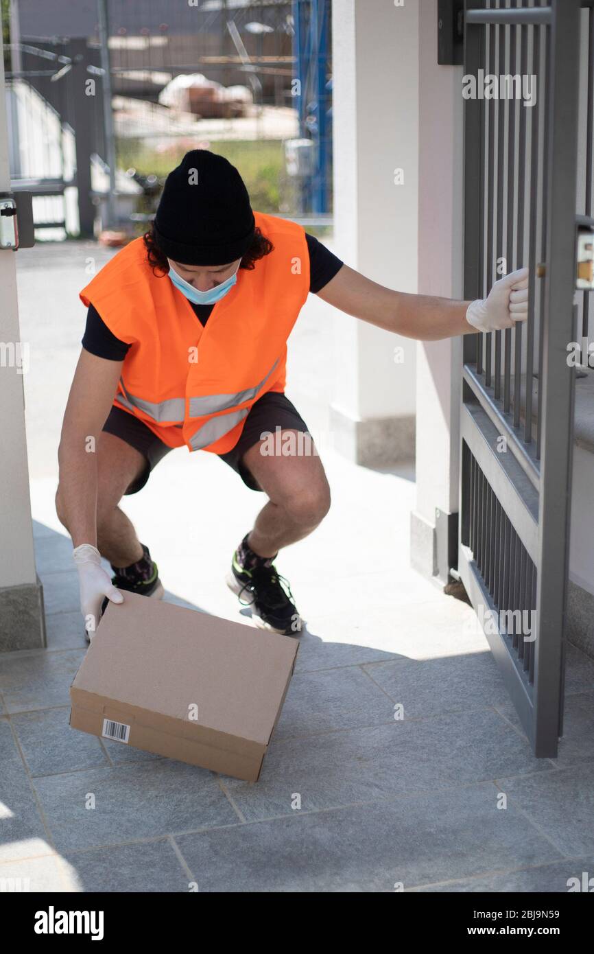 https://c8.alamy.com/comp/2BJ9N59/young-delivery-man-leaving-parcel-box-on-the-floor-at-gate-wearing-ppe-gloves-and-face-mask-during-covid-19-pandemic-lockdown-driver-with-package-2BJ9N59.jpg