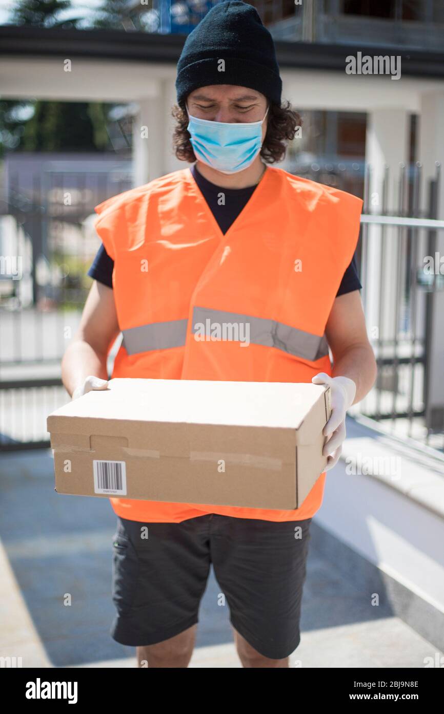 https://c8.alamy.com/comp/2BJ9N8E/young-delivery-man-with-parcel-box-in-outdoor-context-with-ppe-gloves-and-face-mask-during-covid-19-pandemic-lockdown-driver-with-package-outside-2BJ9N8E.jpg