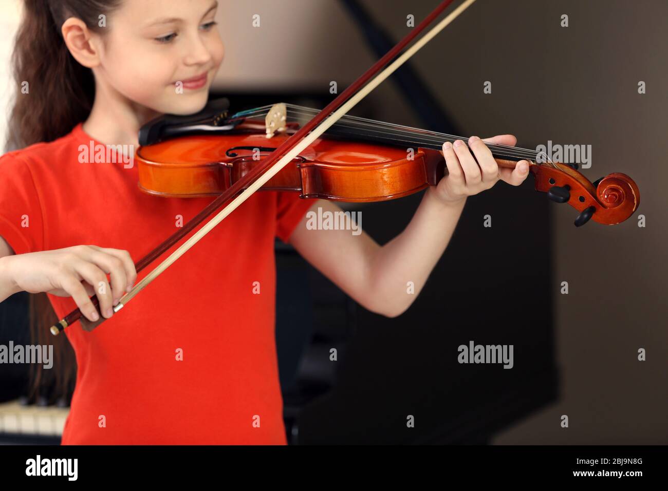 Little girl playing violin on piano background Stock Photo - Alamy