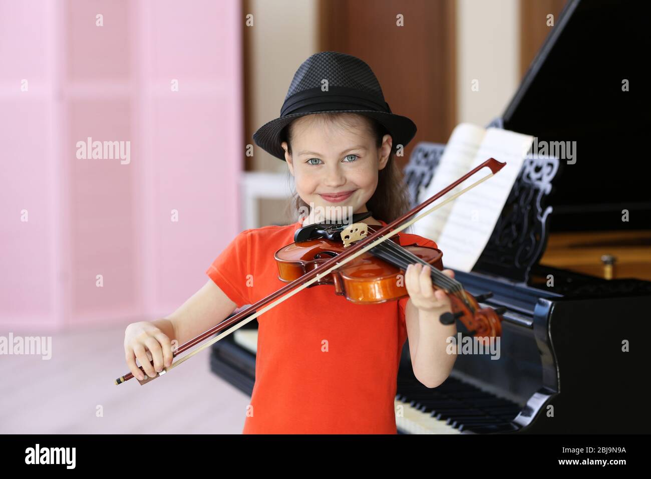 Little girl playing violin on piano background Stock Photo - Alamy
