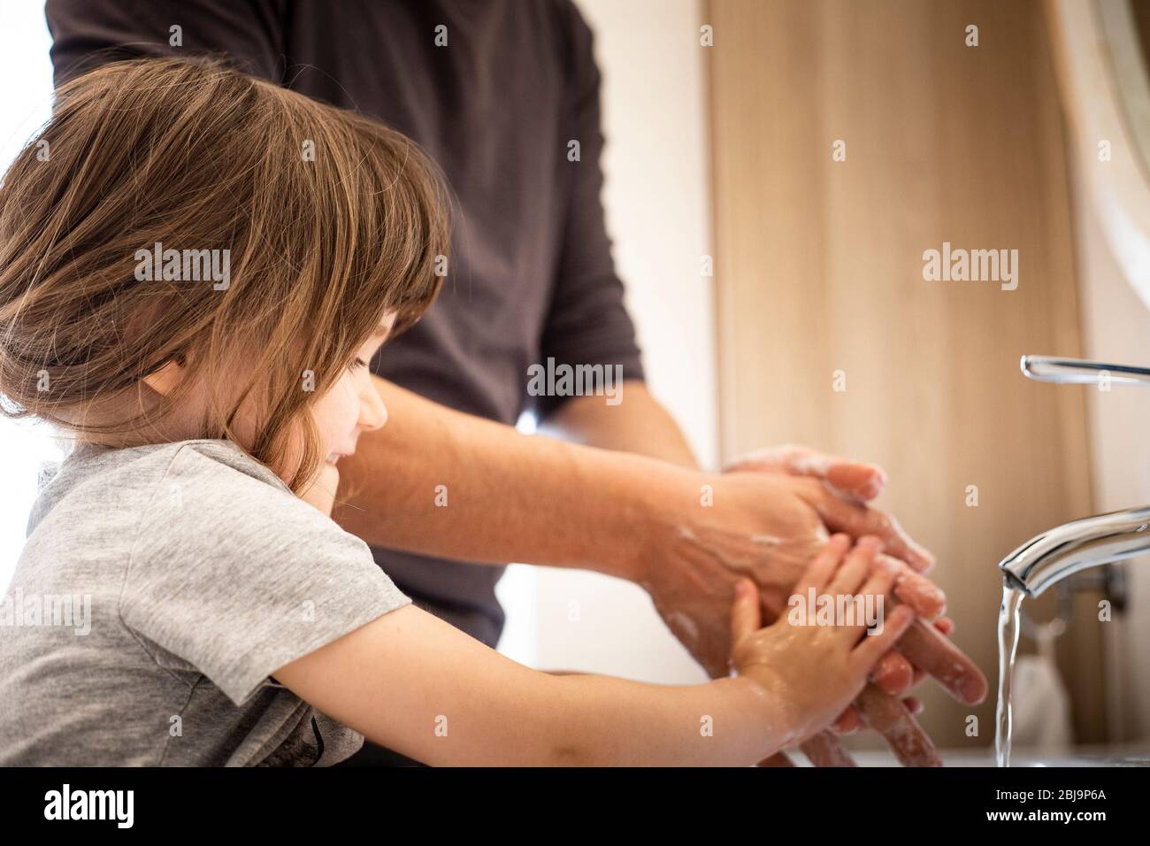 Caucasian father teaching little child girl how to wash hands in bathroom during covid-19 pandemic lockdown. Dad and baby daughter washing hands at si Stock Photo