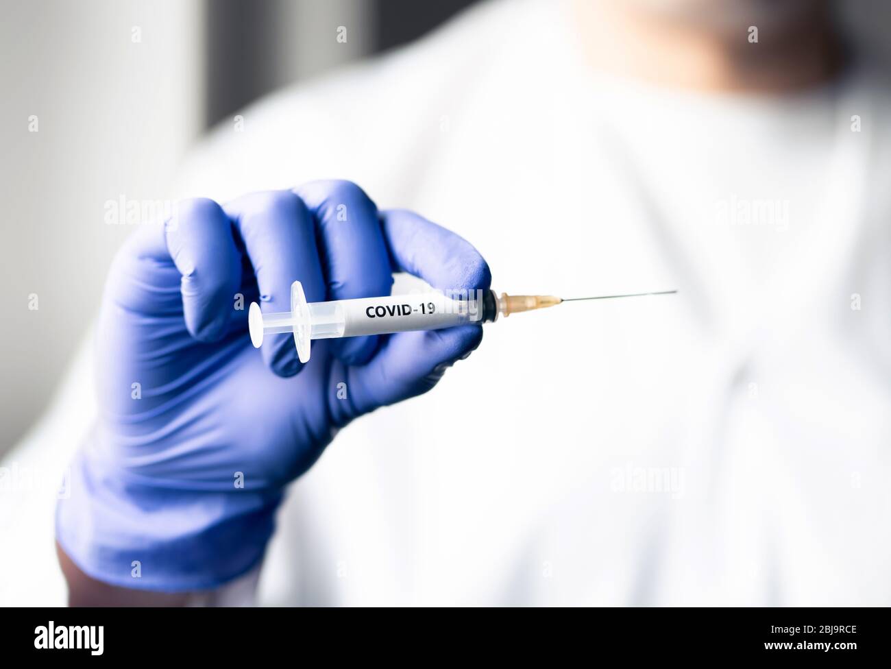 Doctor with coronavirus vaccine needle. Covid 19 shot concept. Virus immunity research in lab. Nurse wearing gloves in hospital. Injection equipment. Stock Photo