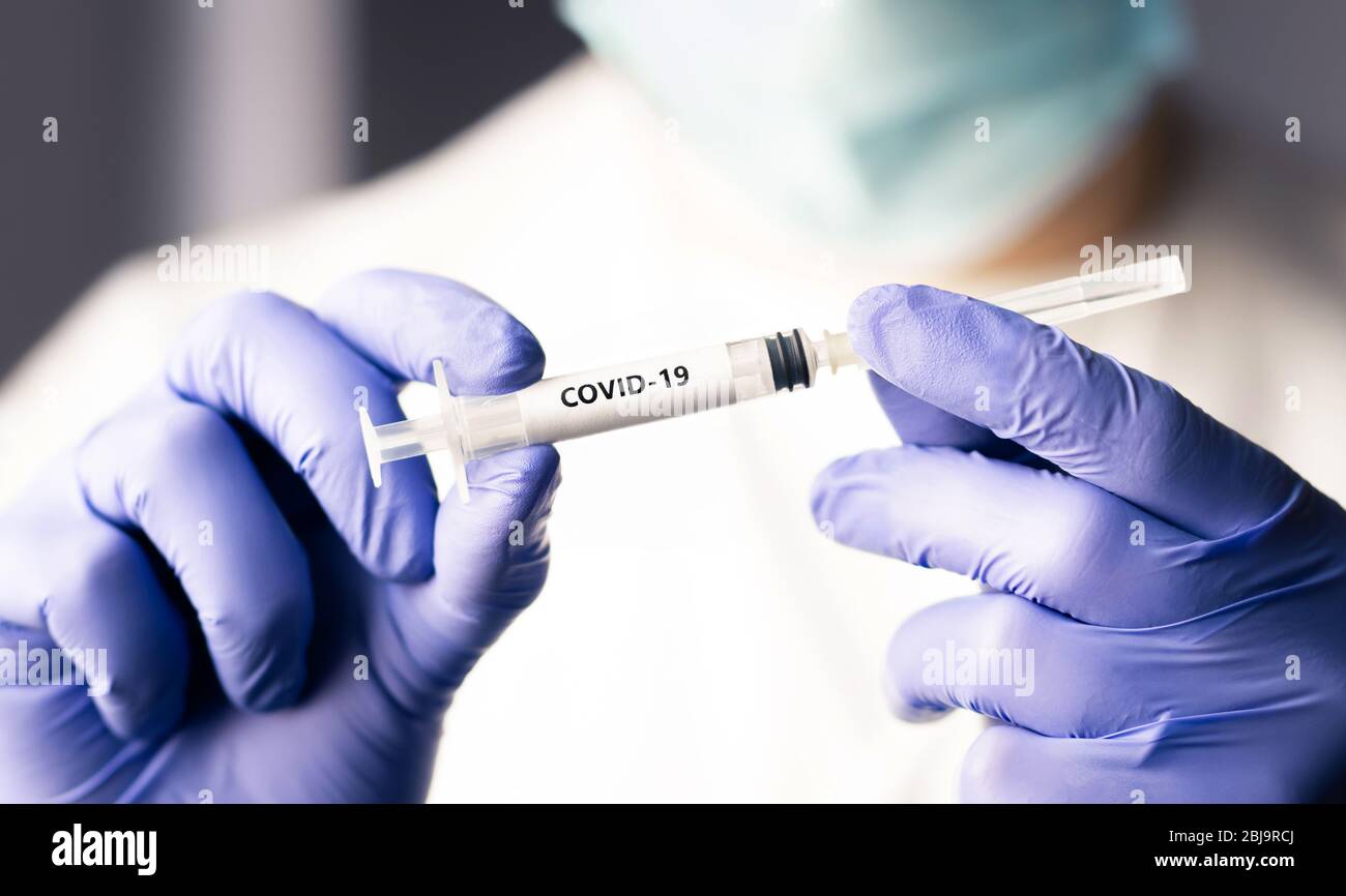 Covid 19 vaccine, immunity and medical treatment concept. Coronavirus syringe and needle. Doctor or nurse working in health care wearing a mask. Stock Photo