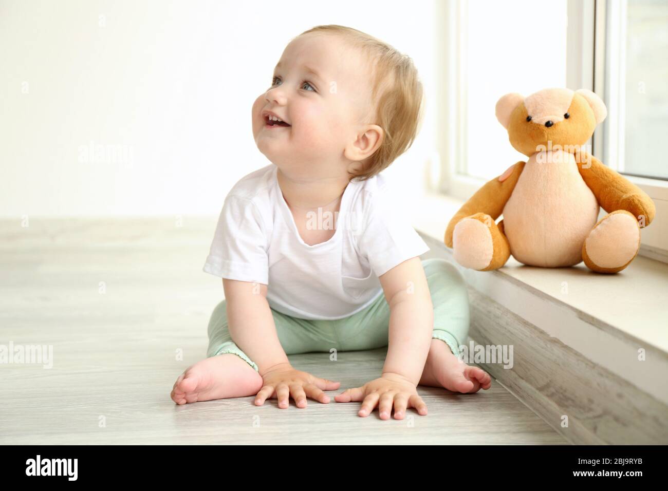 Baby sitting with teddy bear at window in room Stock Photo - Alamy
