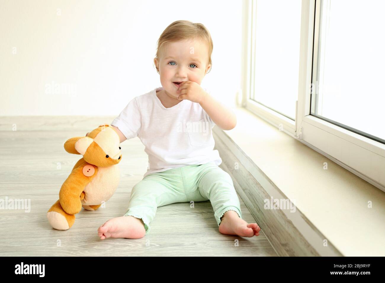 Baby sitting with teddy bear at window in room Stock Photo - Alamy
