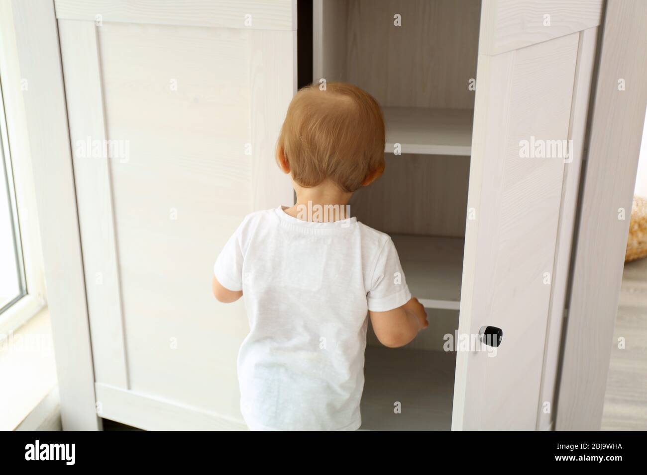 Cute baby girl playing with a wooden cupboard Stock Photo Alamy
