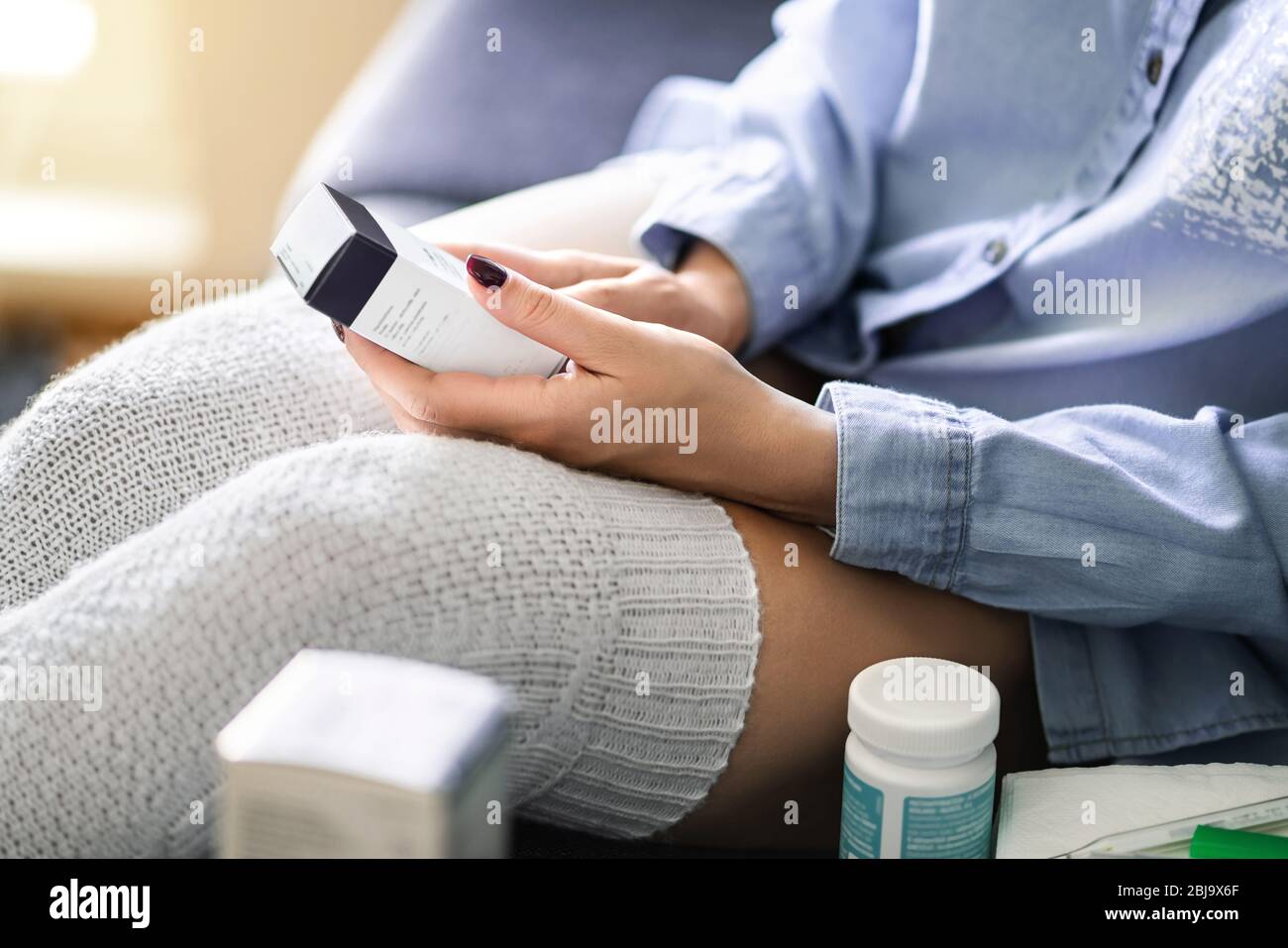 Medicine for flu, virus or pain. Ill woman reading label information of a medical product. Medication for cough and recovery. Sick unwell person. Stock Photo