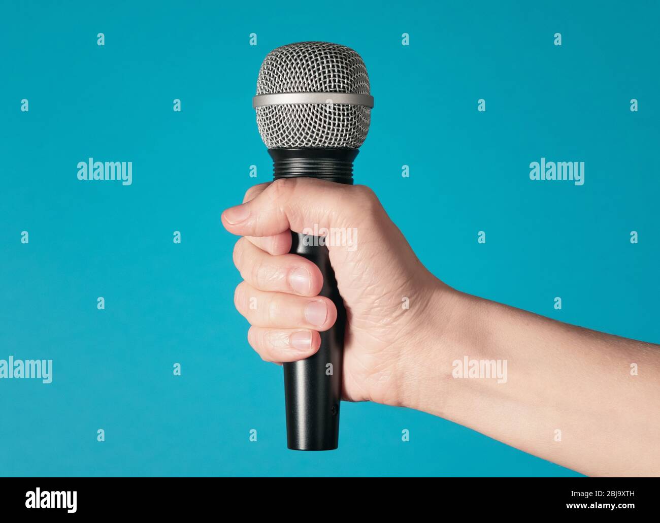 Hand holding up a microphone isolated against a bright blue background Stock Photo