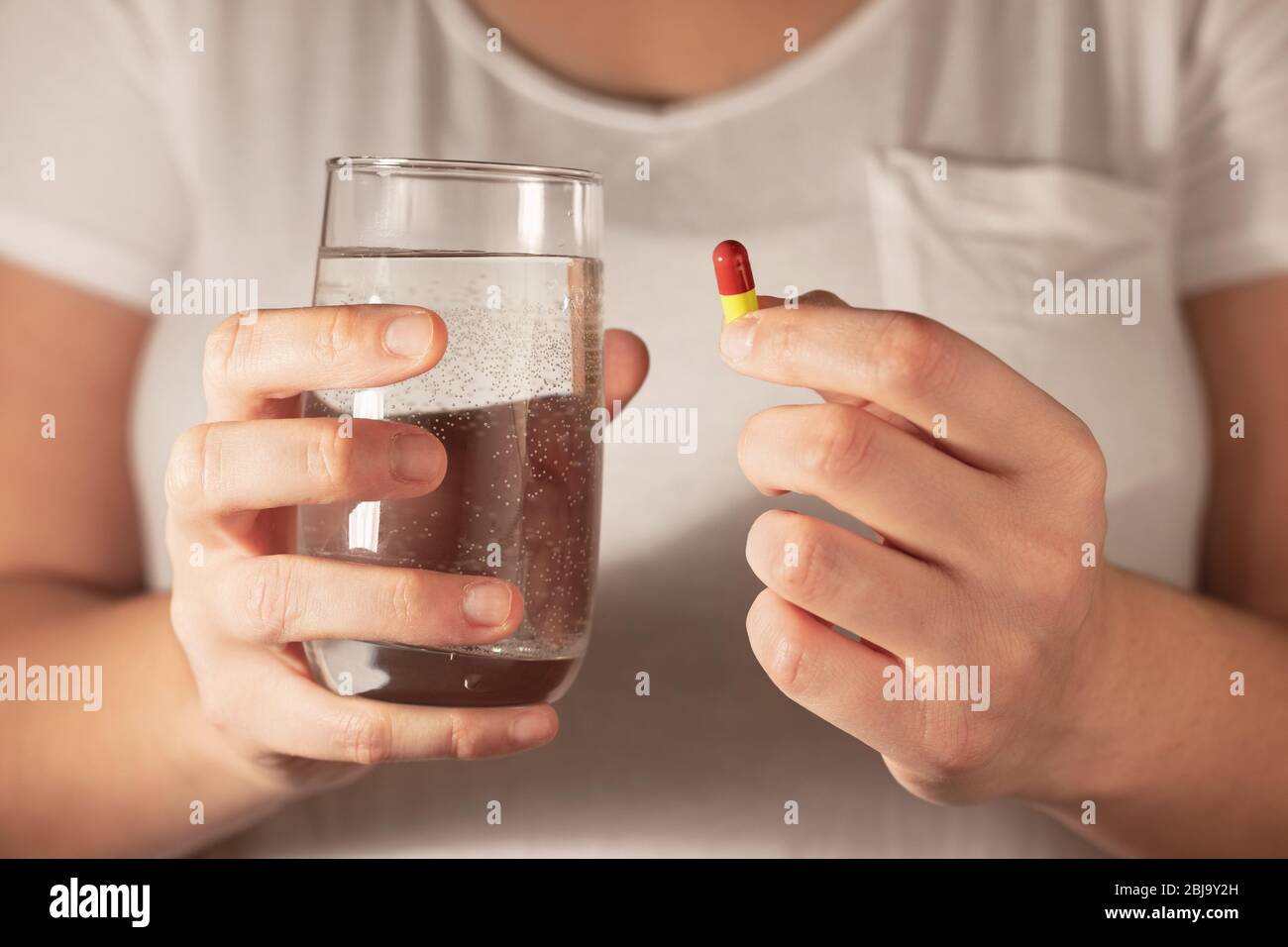 Closeup of a woman holding a medicine pill and a glass of water Stock Photo