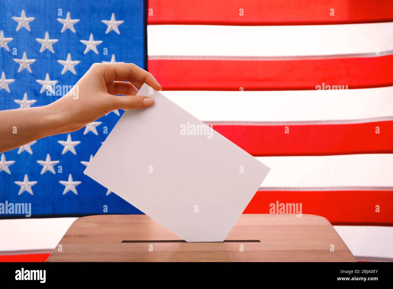 Hand putting down voting paper into a ballot box on American flag ...
