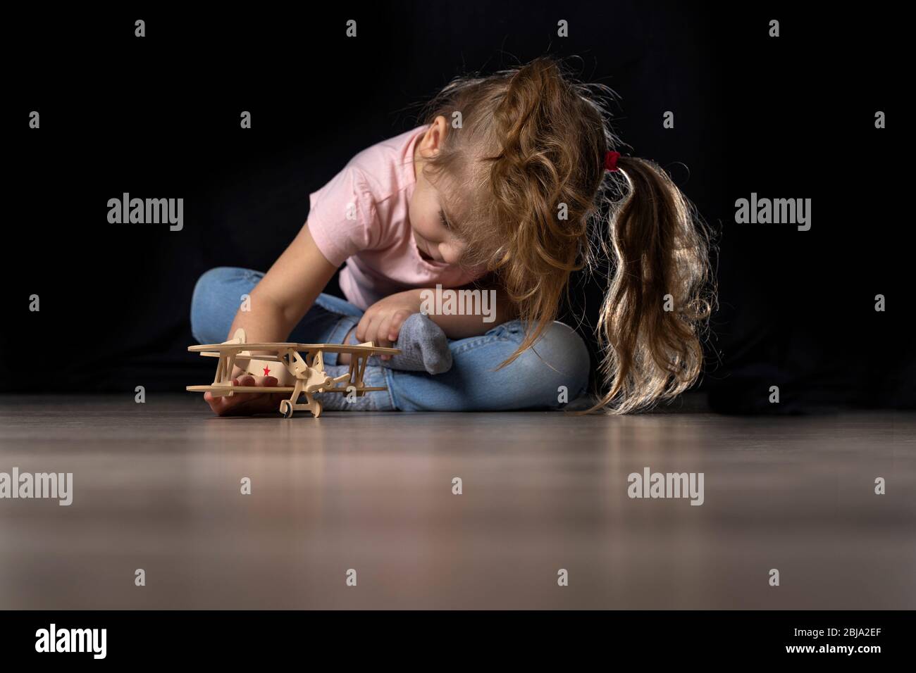 stay home save life text on dark background. sitting next to the floor is a little girl in jeans and playing with a wooden airplane. the need to stay Stock Photo