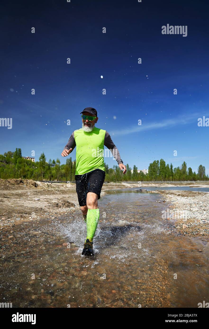 Man with grey beard running on the river with splashes in the morning. Healthy lifestyle concept Stock Photo