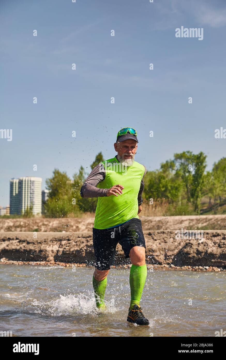 Man with grey beard running on the river with splashes in the morning. Healthy lifestyle concept Stock Photo