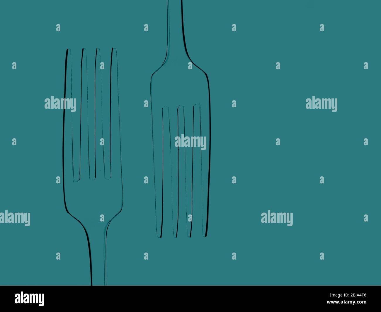 Two dining forks, photographed silhouette outlines on teal green plain background. Stock Photo