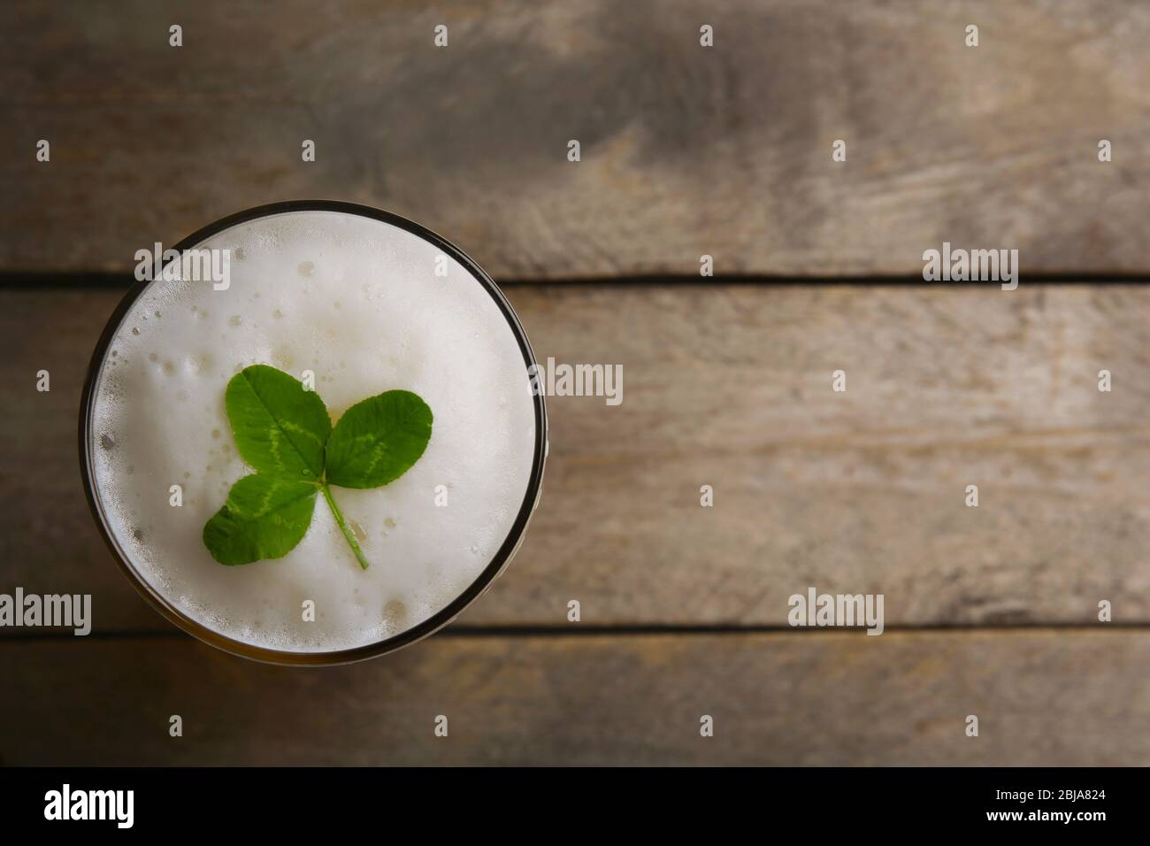 Glass of beer with clover leaf on wooden background Stock Photo